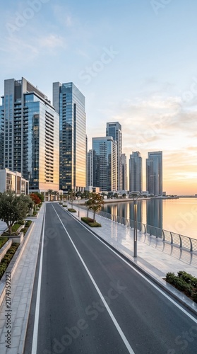 Modern cityscape with glass skyscrapers a waterfront promenade and a street at sunrise