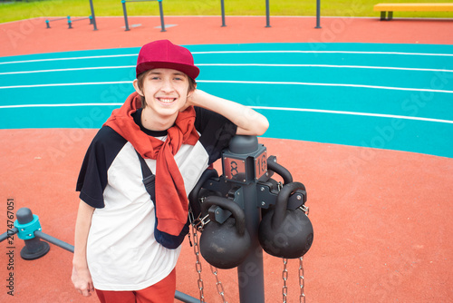 Konstfotografi Happy teenage boy leaning on kettlebell rack on sports ground
