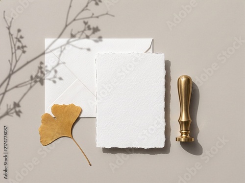 Deckle edge handmade cotton paper card mockup with envelope brass wax stamp and ginkgo leaf on beige plaster