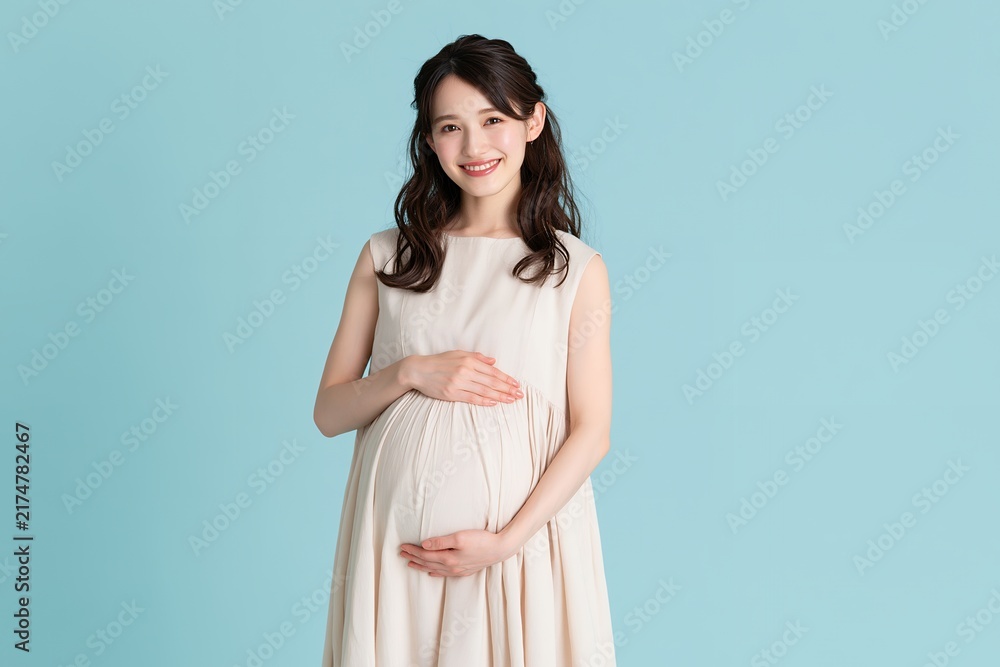 Fototapeta premium 優しい笑顔の日本人妊婦が膨らんだお腹に手を当てるマタニティ