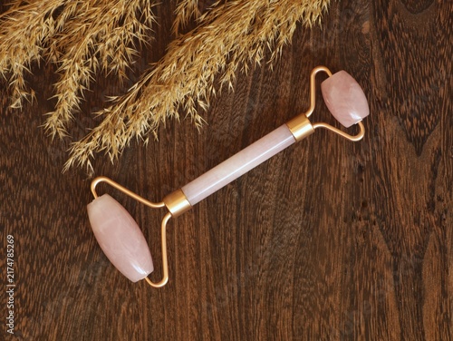 Quadro su tela Rose quartz facial roller with rose gold handle on rustic wooden background with