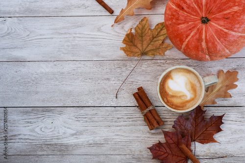 Spicy latte, autumn dry leaves, orange pumpkin on white rustic wooden table top view. November morning vibe, hot drink, coffee shop menu concept