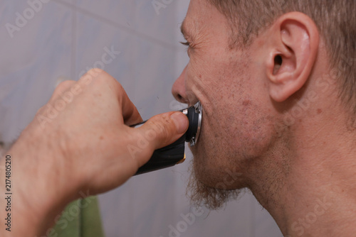 Quadro su tela Man using electric shaver to shave beard in bathroom