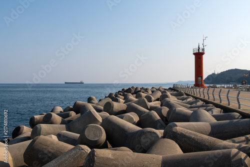 Foto Red Lighthouse and Tetrapod Breakwater with Cargo Ship in Distance