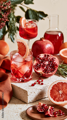 Elegant pomegranate and grapefruit cocktails styled with fresh fruit and herbs on natural stone, luxury wellness self-care beverage composition.