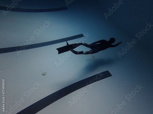 Male freediver silhouette swimming horizontally underwater above pool lane lines