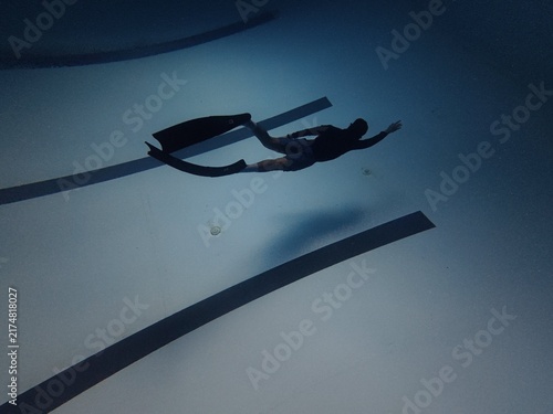 Male freediver gliding underwater above swimming pool lane lines with long fins