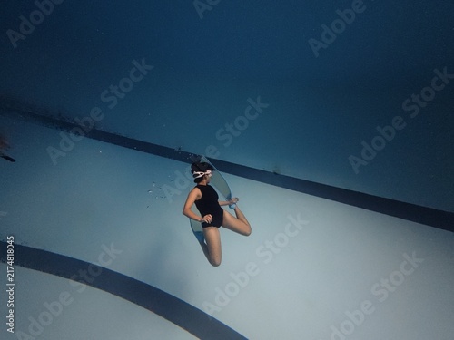 Female freediver floating underwater inside blue swimming pool with long fins