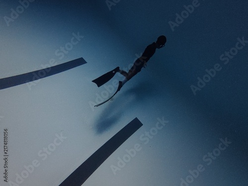 Male freediver kicking long fins underwater above swimming pool lane lines