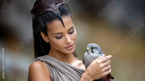 Woman holds a bird of prey while wearing a costume in a natural setting during daylight