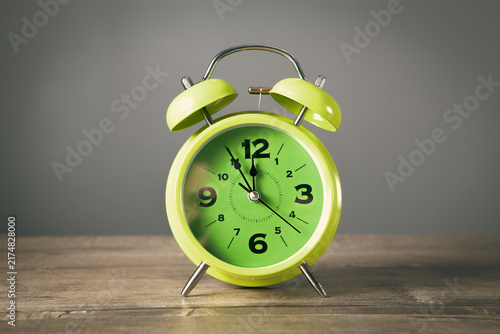 Canvas Print Green alarm clock on wooden table and grey background
