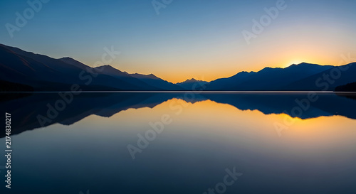 sunrise over calm lake with mountain range mirrored perfectly