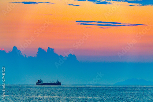Quadro su tela Cargo ship crossing the sea beneath a vivid sunset sky