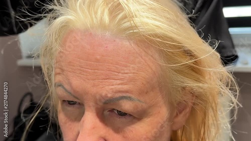 Hairdresser performs a complete blonde transformation by applying bleaching product to hair, washing out the lightener and drying the newly lightened hair in a beauty salon. Close up.