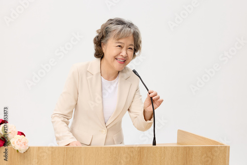 Canvas Print Smiling senior woman speaking at podium during formal presentation
