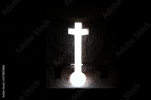 Fotografie Christian cross illuminated by bright light in a dark stone interior