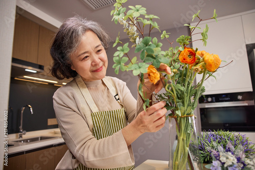Fotografie Senior woman arranging flowers in vase at home kitchen