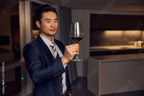 Canvas Print Elegant gentleman examining red wine in modern apartment