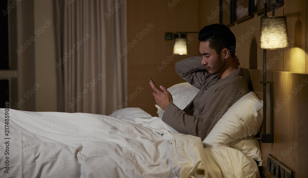 Fototapeta premium Man in Bed Using Phone with Neck Pain at Night