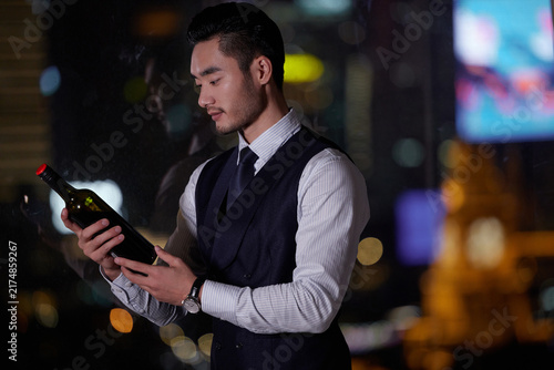 Fotografie Elegant Man Examining Wine Bottle at Night