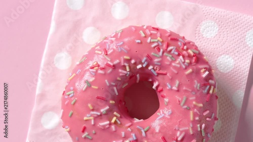 Pink donut rotate on a pink polka dot napkin against a pink background, filmed from above in a clean studio setup. Fresh round pastry presented in a playful colorful composition