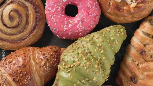 Top view closeup of assortment of freshly baked sweet pastries and buttery croissants, caramel bun, slowly rotating on dark wooden background. Delicious bakery selection for commercial use