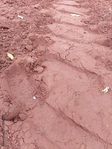 Texture of clumpy red soil with a heavy agricultural vehicle wheel print.