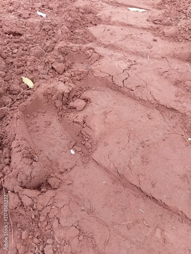 Texture of clumpy red soil with a heavy agricultural vehicle wheel print.
