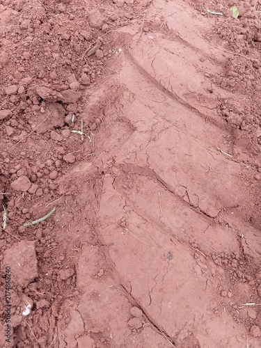 Texture of clumpy red soil with a heavy agricultural vehicle wheel print.