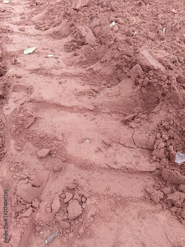 Texture of clumpy red soil with a heavy agricultural vehicle wheel print.