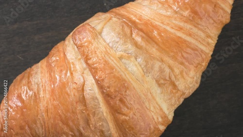 Close-up top view of a freshly baked buttery croissant slowly rotating on a dark wooden table. sweet pastry with soft fluffy texture, beautifully presented on a rustic background