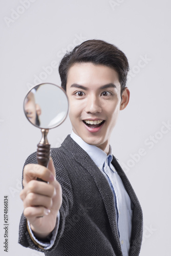 Excited young businessman holding magnifying glass in studio