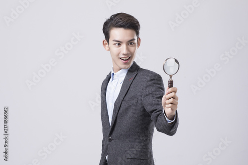 Young businessman holding magnifying glass with surprised expression