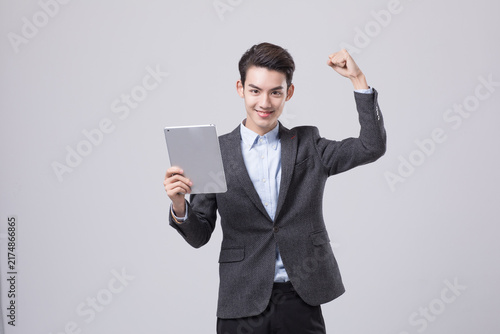 Confident young businessman holding tablet and celebrating success