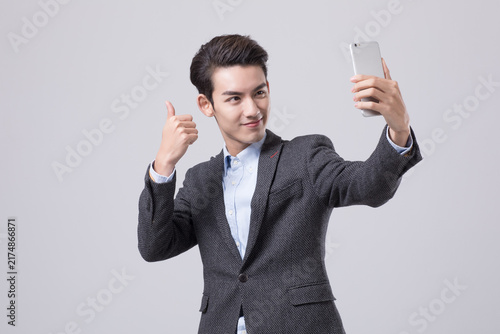 Young businessman taking selfie with smartphone and thumbs up