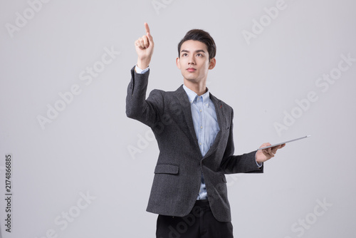 Young businessman holding tablet and pointing upward in studio