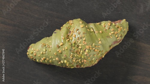 Close-up top view of a freshly baked green pistachio croissant slowly rotating on a dark wooden table. sweet pastry with soft fluffy texture, beautifully presented on a rustic background