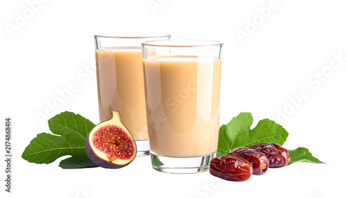 Two clear glasses filled with a beige-colored drink, surrounded by fresh figs, dates, and vibrant green leaves