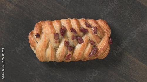 Top view closeup of sweet pecan nut bun rotating on dark rustic wooden  background. Colorful sweet pastry perfect for dessert, bakery, cafe, celebration, social media, and food advertising concepts. 
