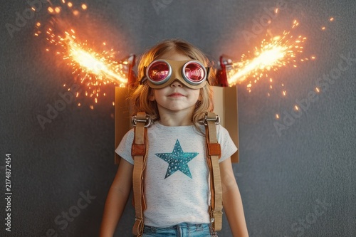 Playful child wearing a cardboard jetpack with bright sparks, star t-shirt and headphones, feeling adventurous and excited