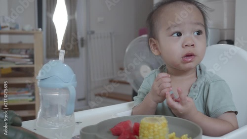 A young child sits at a high chair, curiously engaging with a colorful plate of food. Natural light fills the room, highlighting the joyful atmosphere of mealtime.