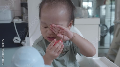 A young child examines a small piece of fruit with a playful expression while sitting in a high chair. The scene captures the wonder of discovering new tastes and experiences in a cozy environment.