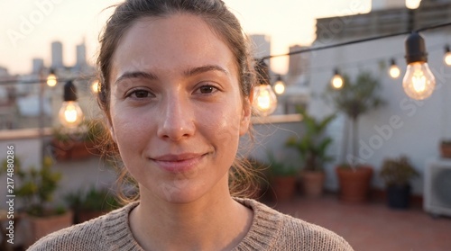 A young woman with a natural smile stands on a rooftop terrace during the golden hour with standing outdoor rooftop