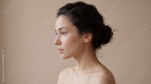 Profile view of a young woman with dark hair looking forward against a neutral beige wall background with looking straight ahead