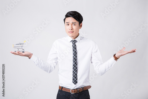 Bild auf Leinwand Confused businessman holding miniature shopping cart and shrugging