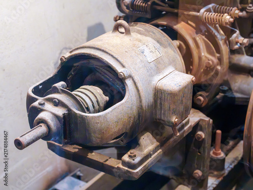 Close-up of a vintage industrial electric motor with rusted metal housing. Detailed view of old mechanical components, shafts, and bolts in a factory setting. Antique heavy machinery equipment.
