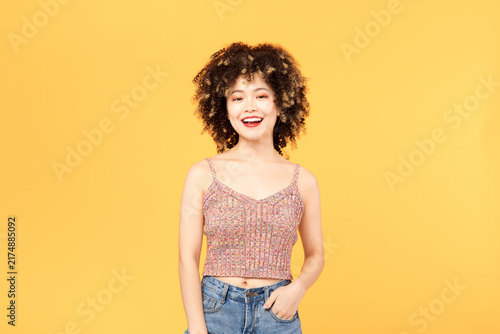 Foto Smiling young woman with curly hair on yellow background