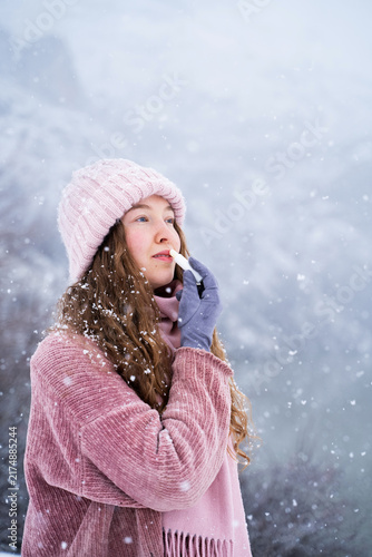 Foto Close-up portrait of a young woman applying lip balm during a snowy winter day