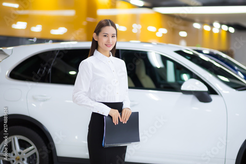 Fotografía Smiling car sales consultant standing by white SUV in showroom
