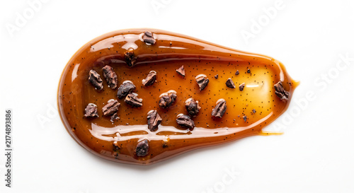 Macro shot of glossy caramel balm swatch with roasted cacao nibs on white background